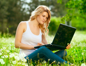 Frau sitzt mit Laptop auf der Wiese