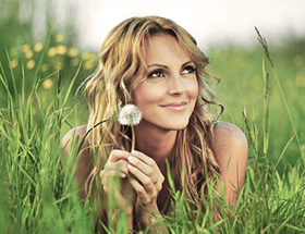 Frau liegt auf der Wiese, lächelt und hält eine Blume in der Hand